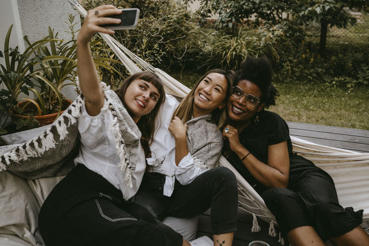 Smiling young woman taking selfie with friends through mobile phone during garden party
