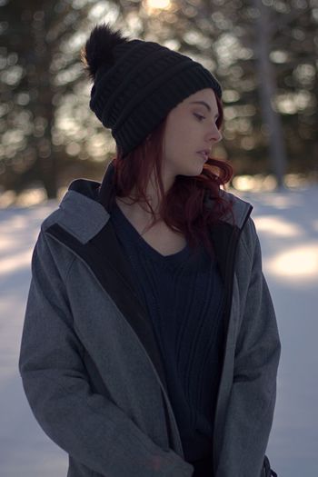 Thoughtful young woman looking away while standing in forest during winter