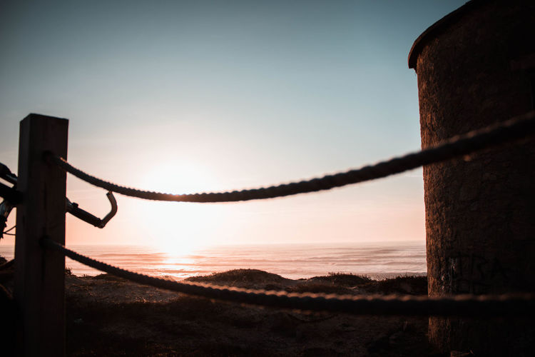 Silhouette of wooden post on beach against sky during sunset
