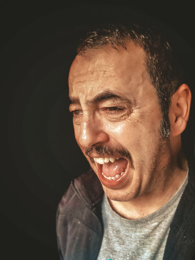 Close-up of man shouting against black background