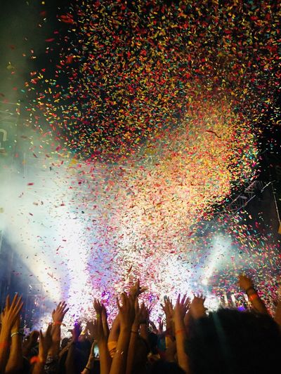 People with arms raised against confetti flying during music concert