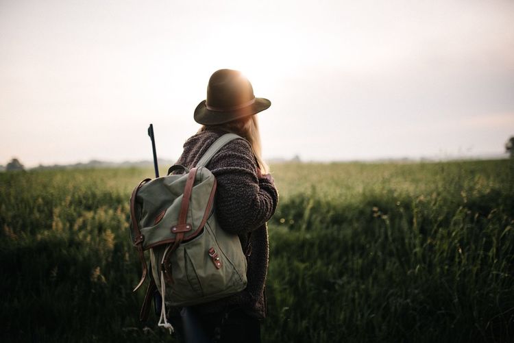 Side view of woman with backpack standing on land against sky at sunset