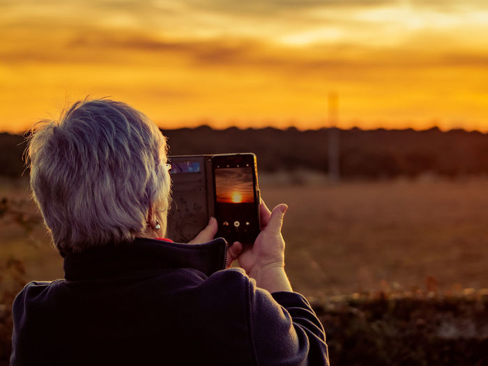 Rear view of woman photographing with mobile phone against orange sky