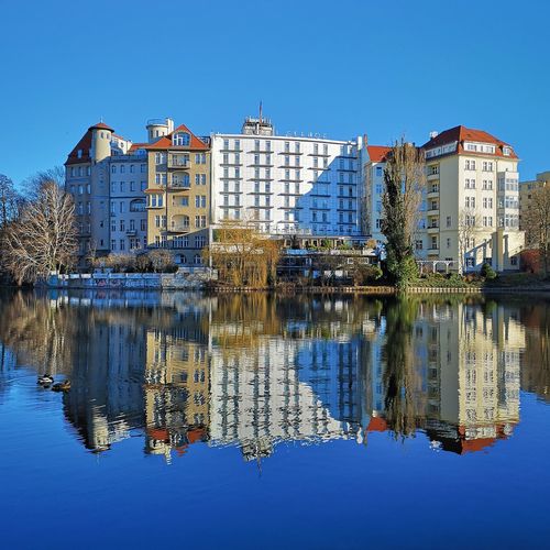 Reflection of buildings in lake against clear blue sky