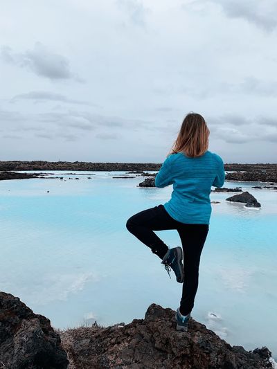 Rear view of woman doing yoga on rock by blue lagoon against sky