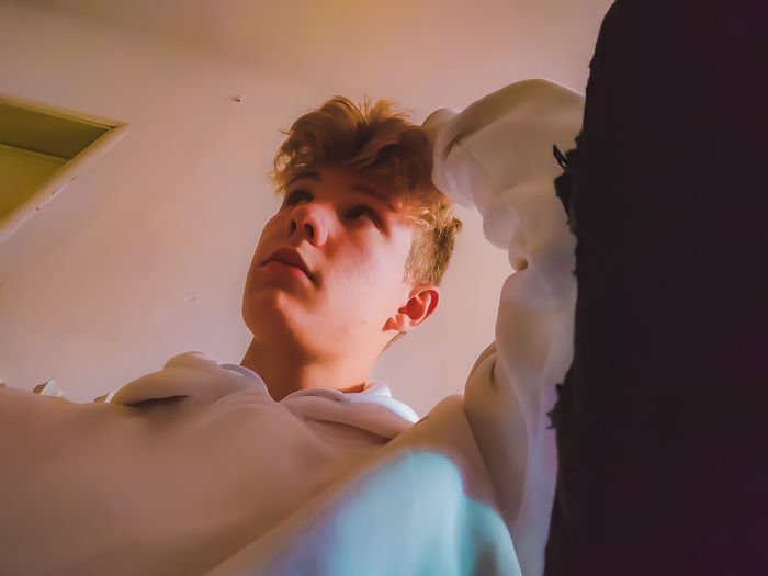 Low angle view of young man looking away sitting at home