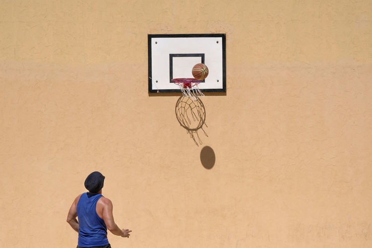 Rear view of man playing basketball against wall