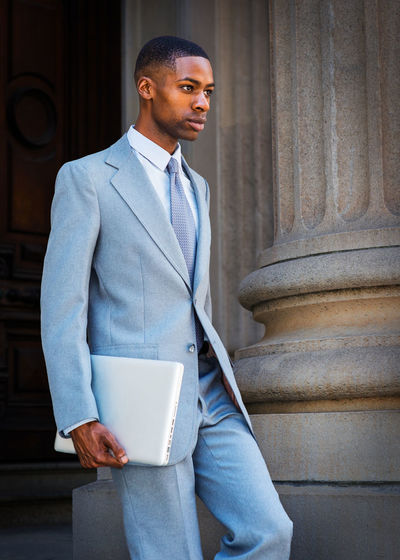 Young african american businessman holding a laptop computer, walking down office building doorway.