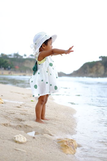 Full length of cute girl standing on sand at beach against sky