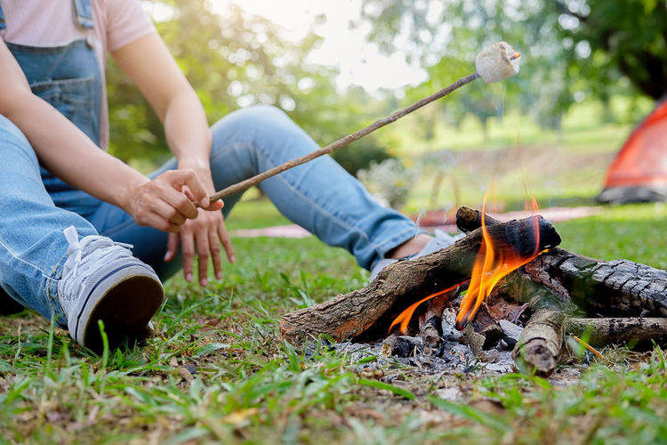 Low section of woman roasting marshmallow on campfire