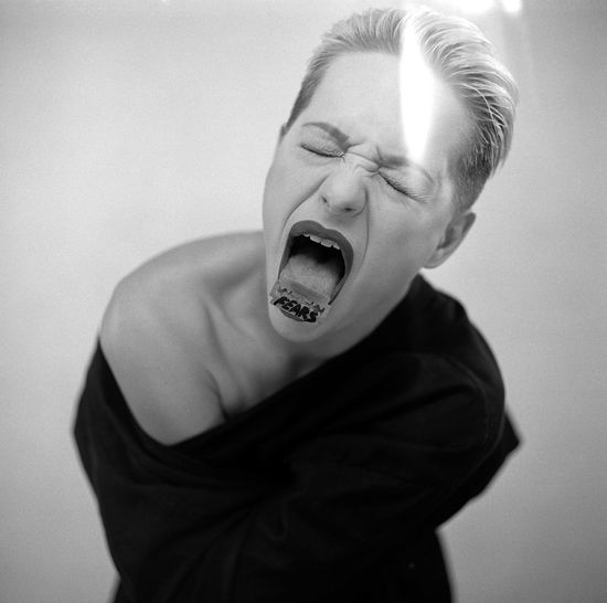 Young woman with blade on tongue screaming against white background