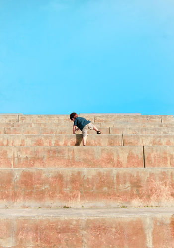 Full length rear view of boy climbing steps against clear blue sky