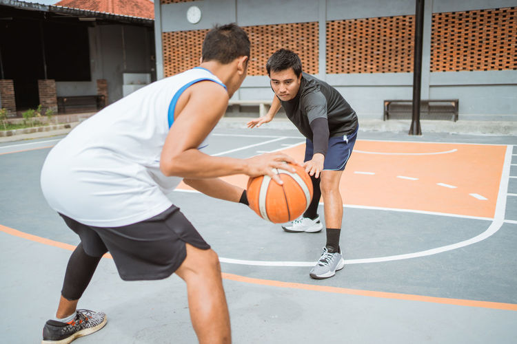Young man playing with ball in basketball court