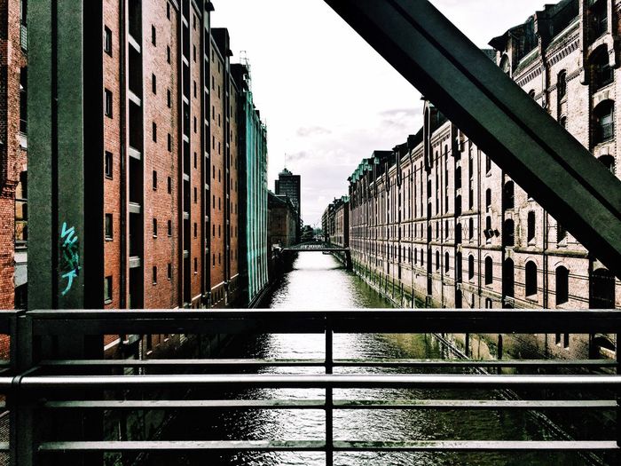 Canal by footbridge in city against sky