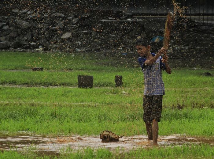 Boy splashing muddy water with cricket bat while standing on field