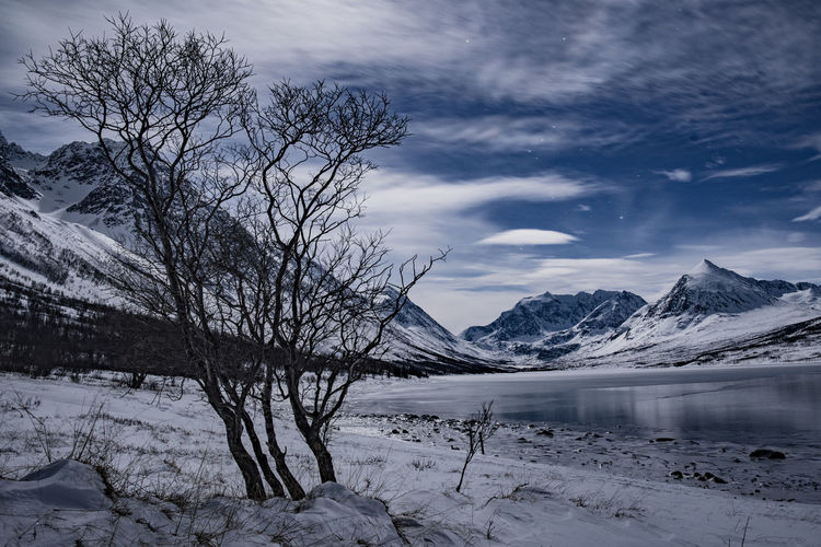 Scenic view of frozen lake by snowcapped mountains against sky