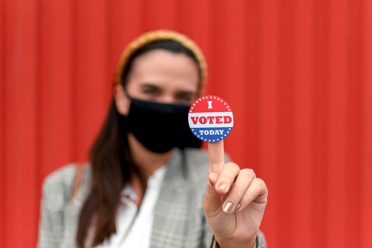 Selective focus of woman with face mask holding voting sticker, i voted, election, vote.