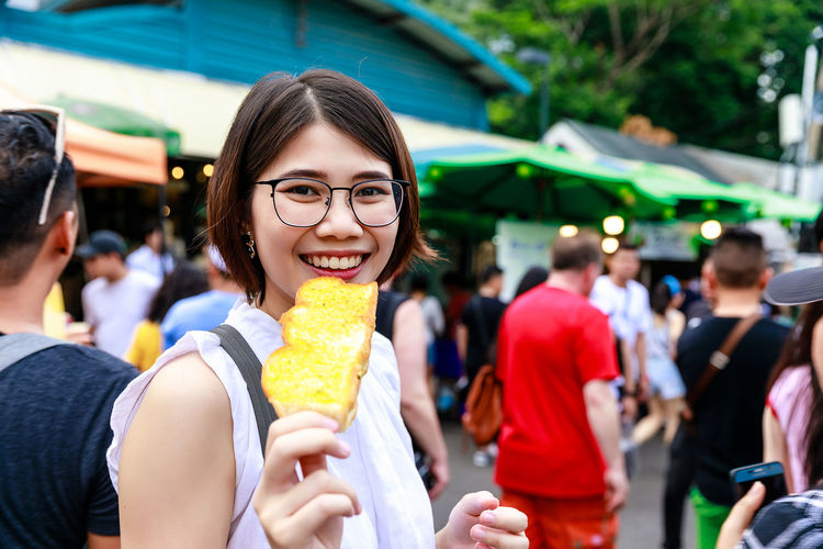 Asian young short hair beautiful woman wearing glasses enjoy eating butter toast at street market