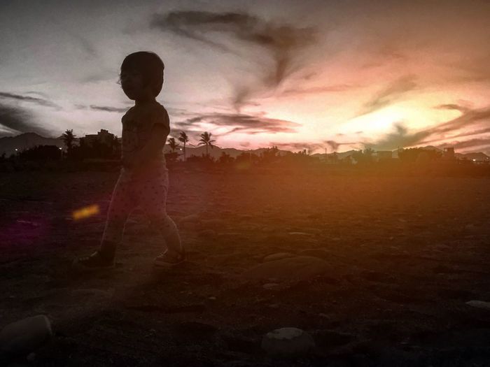 Silhouette boy standing on landscape against sky during sunset