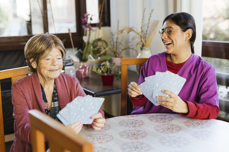Happy healthcare worker playing cards with senior woman at home