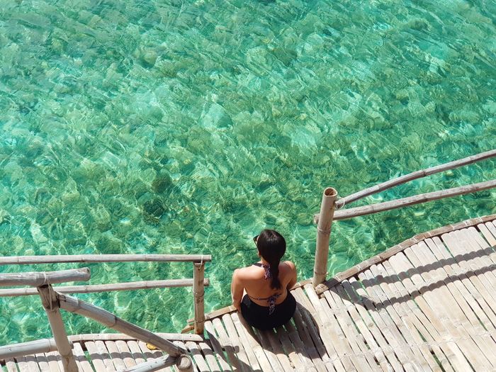 High angle view of woman sitting on pier over sea