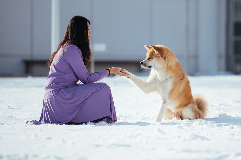 Side view of woman with dog sitting on snow