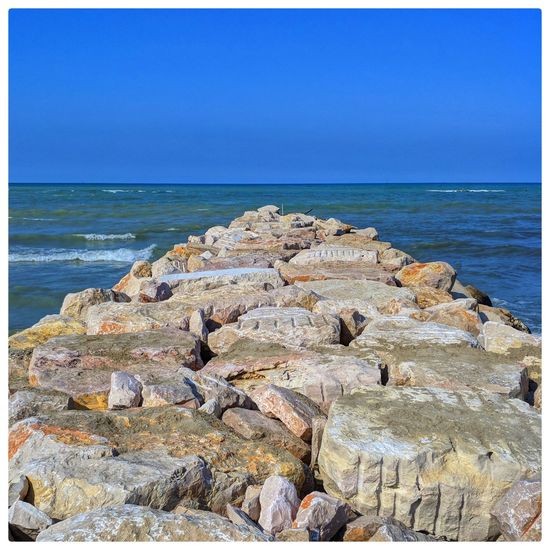 Rocks on beach by sea against blue sky