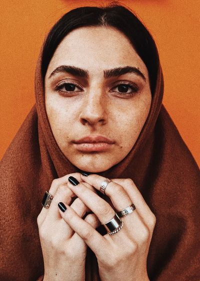 Close-up portrait of woman in hijab against orange background