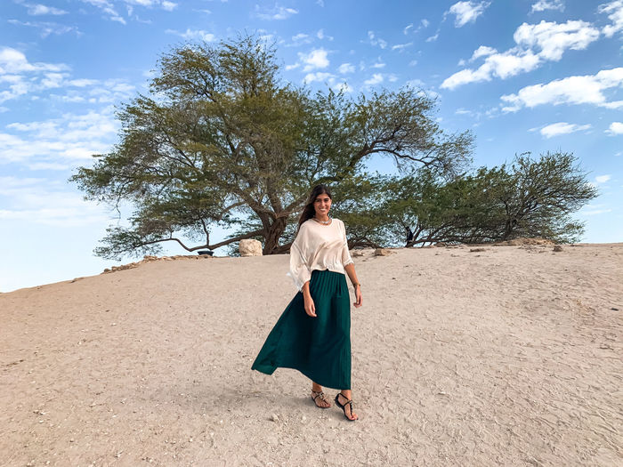 Full length of woman standing by tree on the desert sand against sky