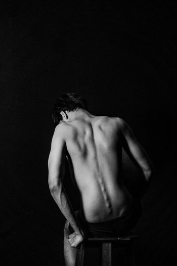 Rear view of naked man on seat against black background