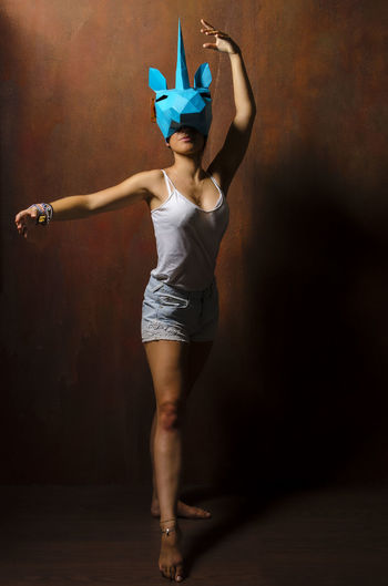 Woman wearing unicorn mask while dancing against wall