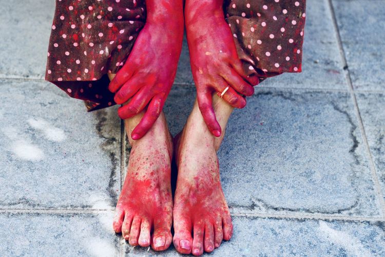 Low section of messy woman sitting on footpath during holi