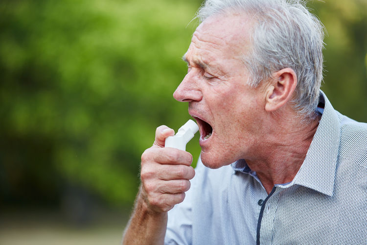 Close-up of senior man using asthma inhaler outdoors