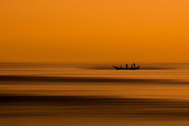 Silhouette boat on sea against orange sky