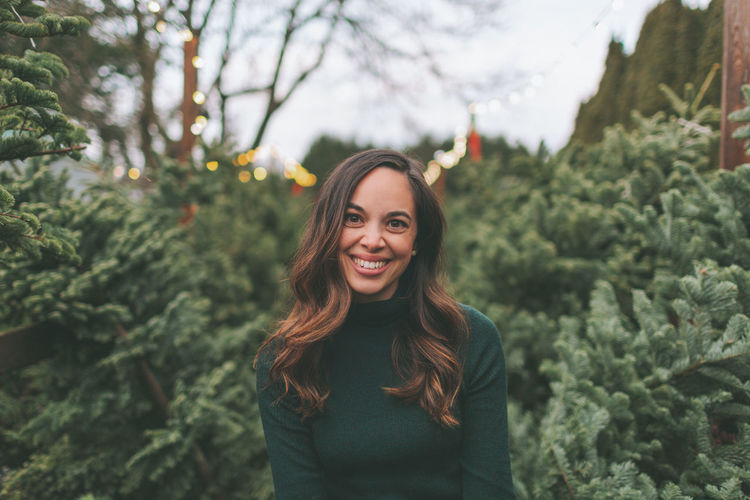 Portrait of a smiling young woman standing against trees