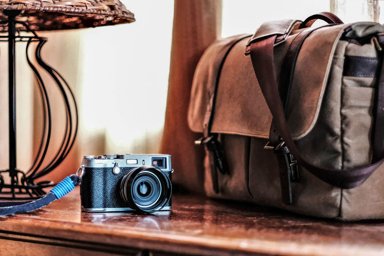 Close-up of camera by bag on wooden table at home