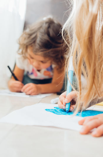 Cute little children girls lying on floor and drawing with color markers.