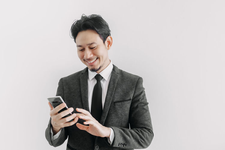 Smiling young man using smart phone against white background