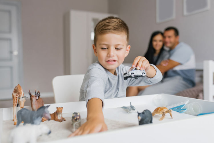 Boy son plays with toys against the background of happy parents at home