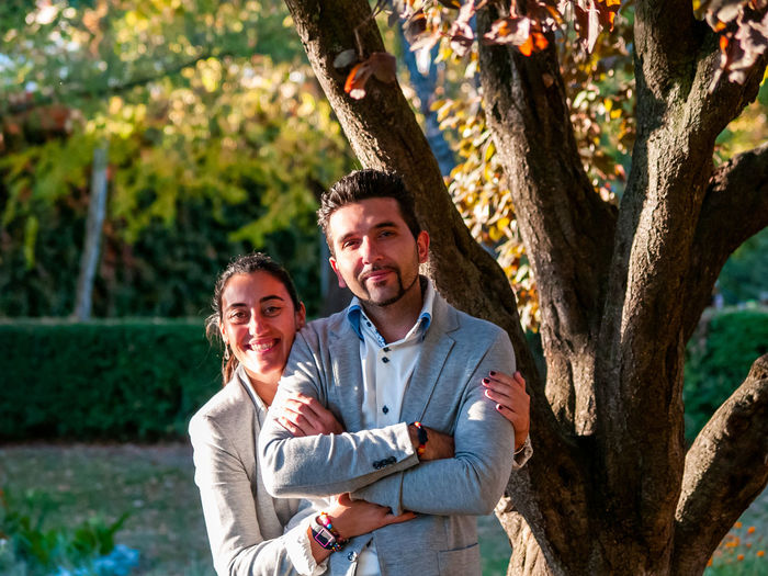 Portrait of smiling couple standing against tree in park