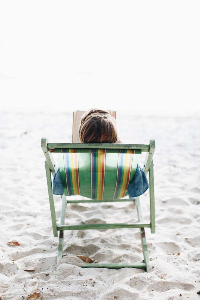 Rear view of woman with book lying on lounge chair at beach
