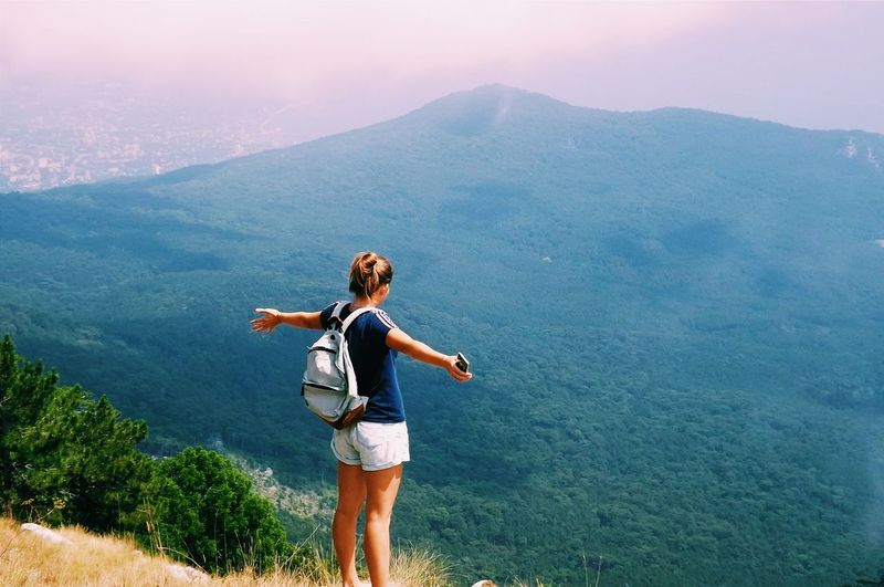 Woman with arms outstretched standing on mountain against sky