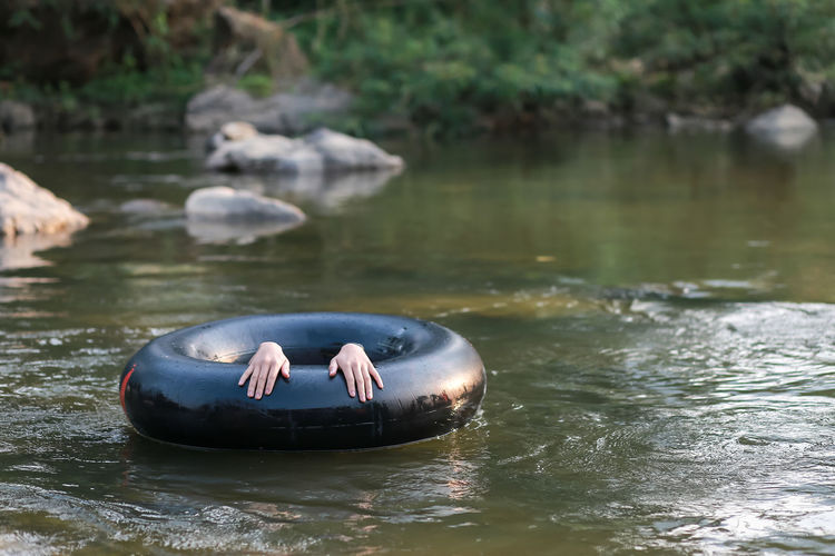 A black rubber ring, a man's hand is floating on the river. a soak relaxing vacation in thailand.