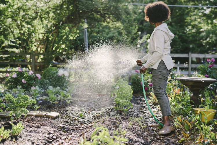 Side view of mature woman watering plants in yard