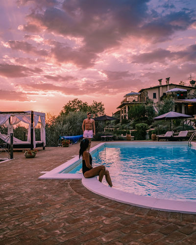 Woman in swimming pool against sky during sunset