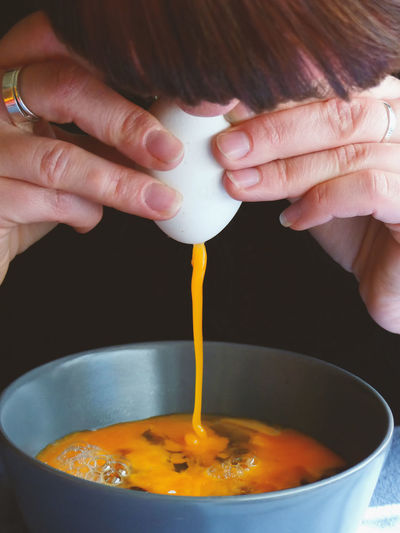 Close-up of woman pouring egg yolk in bowl on table