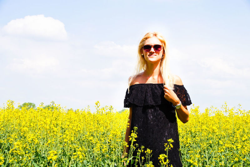 Portrait of smiling young woman standing on oilseed rape field