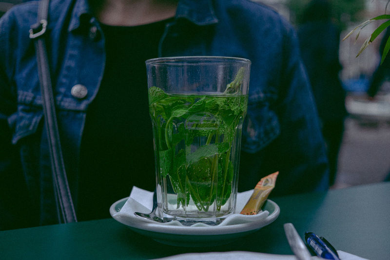 Close-up of drink in glass on table by woman