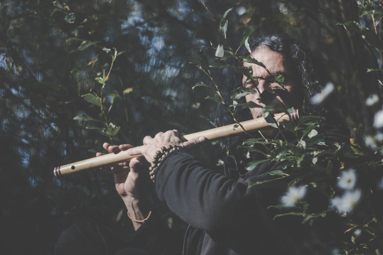 Low angle view of man playing flute while standing in forest
