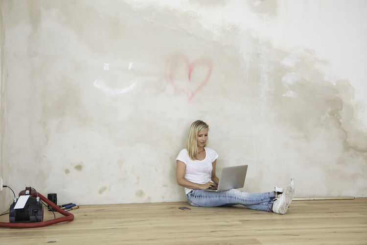 Close-up of young woman sitting on floor using laptop in empty room